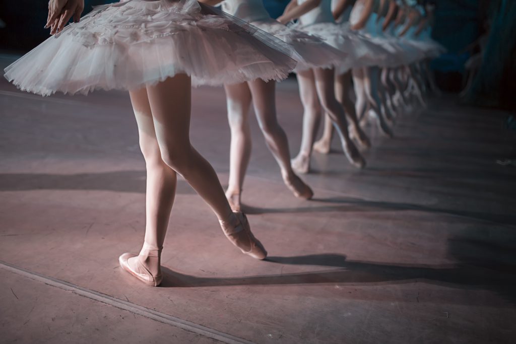 Dancers in white tutu synchronized dancing on stage. Repetition.